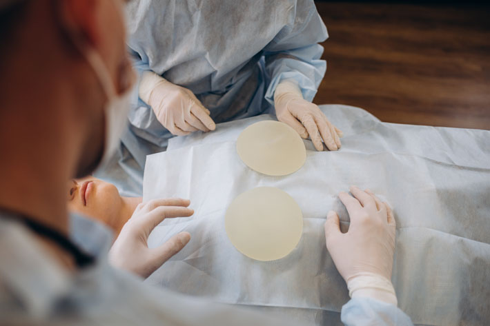 Doctor showing silicone implants for breast augmentation to patient in clinic, closeup. Cosmetic surgery