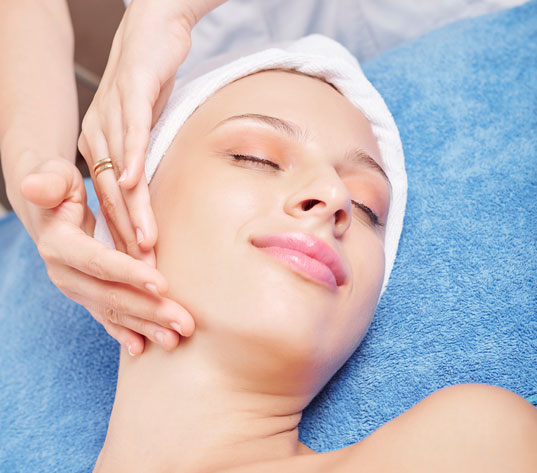 Smiling young Caucasian woman lying on bed and enjoying face lifting massage in beauty salon