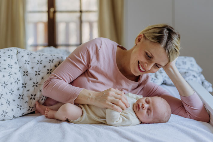 Portrait of cute baby girl being kissed by mother on bed